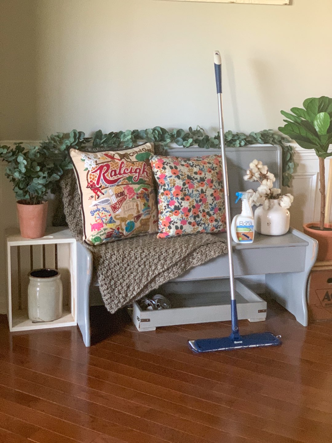 Keeping Our Floors Clean with Bona Essentials - I'm Fixin' To - @mbg0112 | Keeping Our Floors Clean with Bona Essentials by popular lifestyle blog, I'm Fixin' To: image of a bottle of Bona Essentials Hardwood Floor Deep Cleaner and a Bona Essentials Mop next to a grey wooden bench.