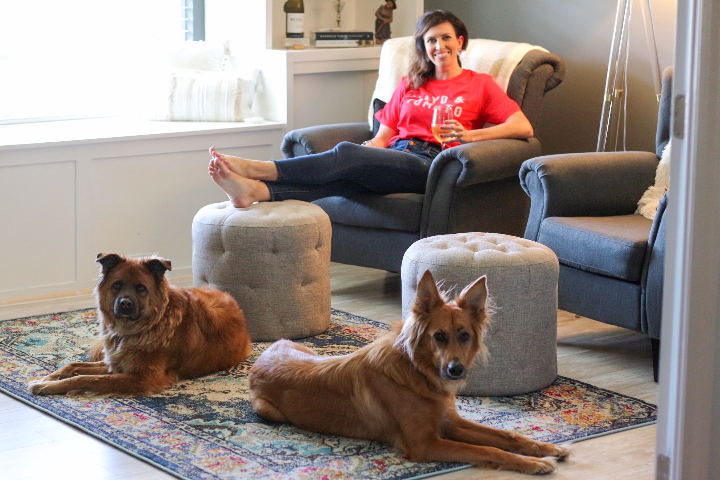How I Make Time for Decorating with Wente Vineyards - I'm Fixin' To - @mbg0112 | How I Make Time for Decorating with Wente Vineyards by popular North Carolina lifestyle blog, I'm Fixin' To: image of a woman sitting in a grey arm chair with her feet up on an ottoman and holding a glass of Wente Vineyards wine while her two dogs sit on the floor nearby.