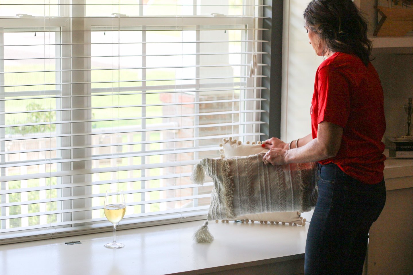 How I Make Time for Decorating with Wente Vineyards - I'm Fixin' To - @mbg0112 | How I Make Time for Decorating with Wente Vineyards by popular North Carolina lifestyle blog, I'm Fixin' To: image of a woman rearranging some throw pillows on her window bench with a glass of Wente Vineyards wine close by