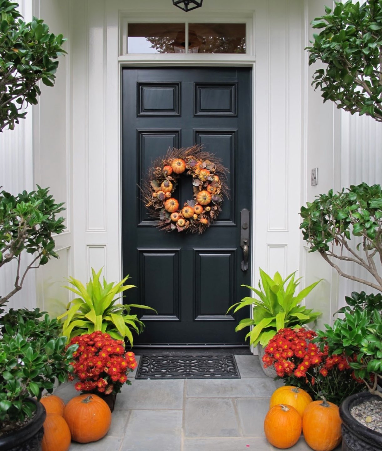 Inspiration Board: Fall Front Porch Ideas - I'm Fixin' To - @mbg0112 | Inspiration Board: Fall Front Porch Ideas by popular North Carolina life and style blog, I'm Fixin' To: image of a front porch decorated with a fall wreath, pumpkins and potted red mums.
