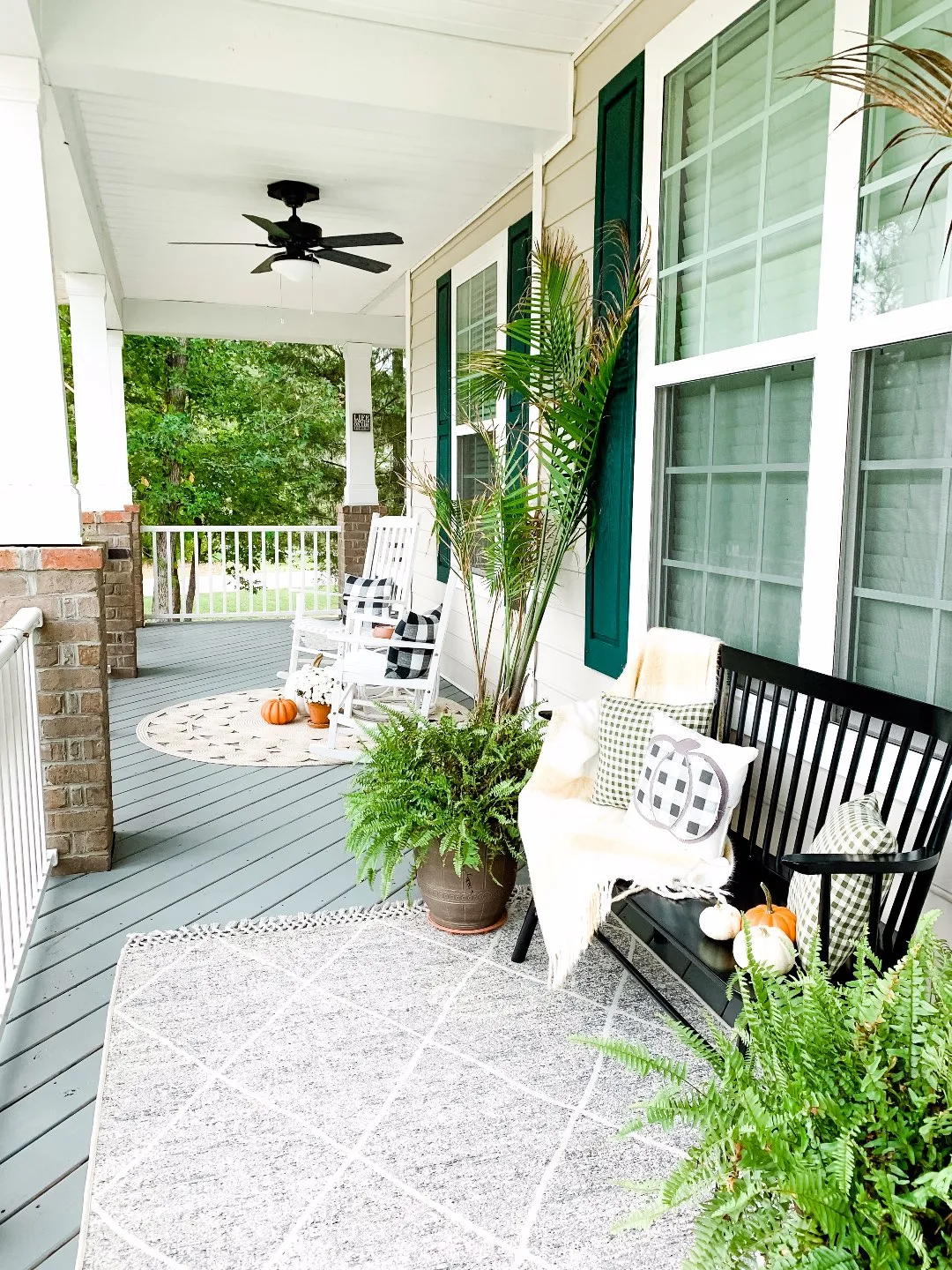 Our Inviting and Cozy Fall Front Porch Decor Ideas - I'm Fixin' To - @mbg0112 | Our Inviting and Cozy Fall Front Porch Decor Ideas by popular North Carolina lifestyle blog, I'm Fixin' To: image of a front porch decorated with a Target Opalhouse Desert Hatch Outdoor Rug Gray, Amazon Jerimiah Spindleback BenchAmazon 4TH Emotion Set of 2 Farmhouse Buffalo Check Plaid Throw Pillow Covers, Target Smith and Hacken 12" Iron Galvanized Planters, Target Threshold 22" Artificial Berry Wreath White, pumpkins, Target Smart Living San Rafael II 15" LED Solar Mission Outdoor Lanterns, Hayneedle Coral Coast Indoor/Outdoor Mission Slat Rocking Chairs, mums, and green plants. 