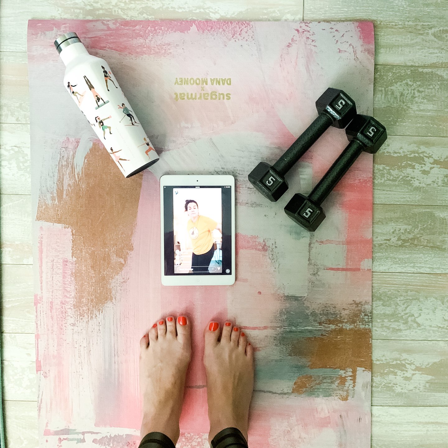 How to Stay Active at Home by popular NC lifestyle blog, I'm Fixin' To: image of a woman standing on a yoga mat that has a white metal water bottle, 5 lbs hand weights, and a ipad on it.