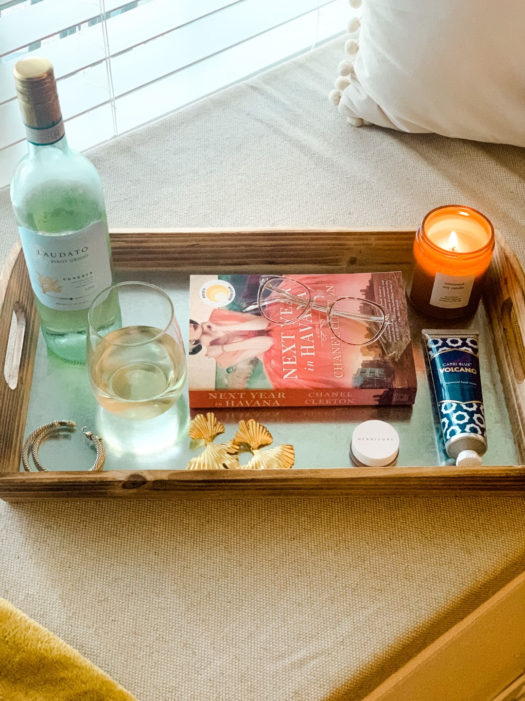 Top 10 Best Wines by popular N.C. lifestyle blog, I'm Fixin' To: image of a bottle of Laudato Pinot Grigio on a serving tray next to a book, some gold earrings, and a lit candle.