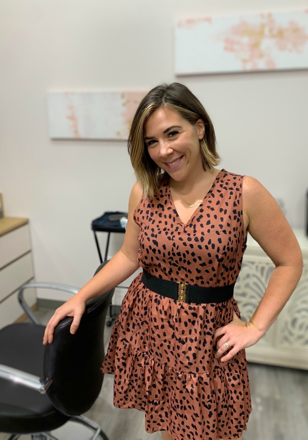 Salon Lofts Falls of Neuse Olive Park by popular N.C. lifestyle blog, I'm Fixin' To: image of a woman wearing a brand and black dot dress with a black belt while standing next to a salon chair. 