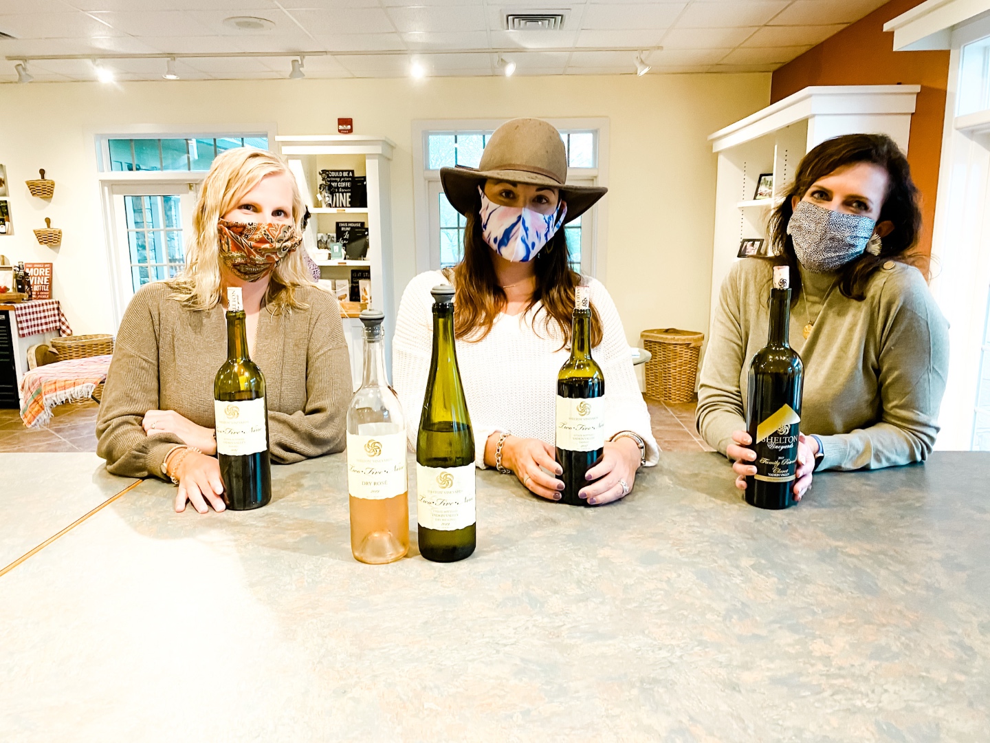 Western NC Wineries: 6 Wineries to Visit During your Next Girls' Weekend - I'm Fixin' To - @mbg0112 |Western NC Wineries by popular NC blog, I'm Fixin' To: image of a woman and two of her friends sitting infront of bottles of wine at Shelton Vineyards. 