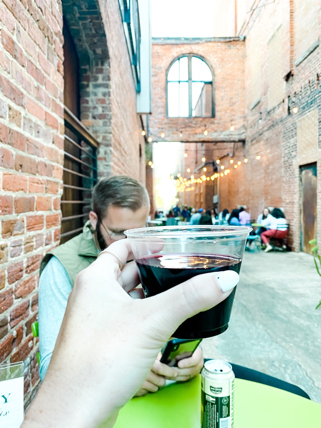 2020, a Year in Review: our Travel Adventures - I'm Fixin' To - @imfixintoblog |Year in Review by popular NC travel blog, I'm Fixin' To: image of a woman sitting at a table in an alley way decorated with bistro lights and holding a plastic cup of red wine.