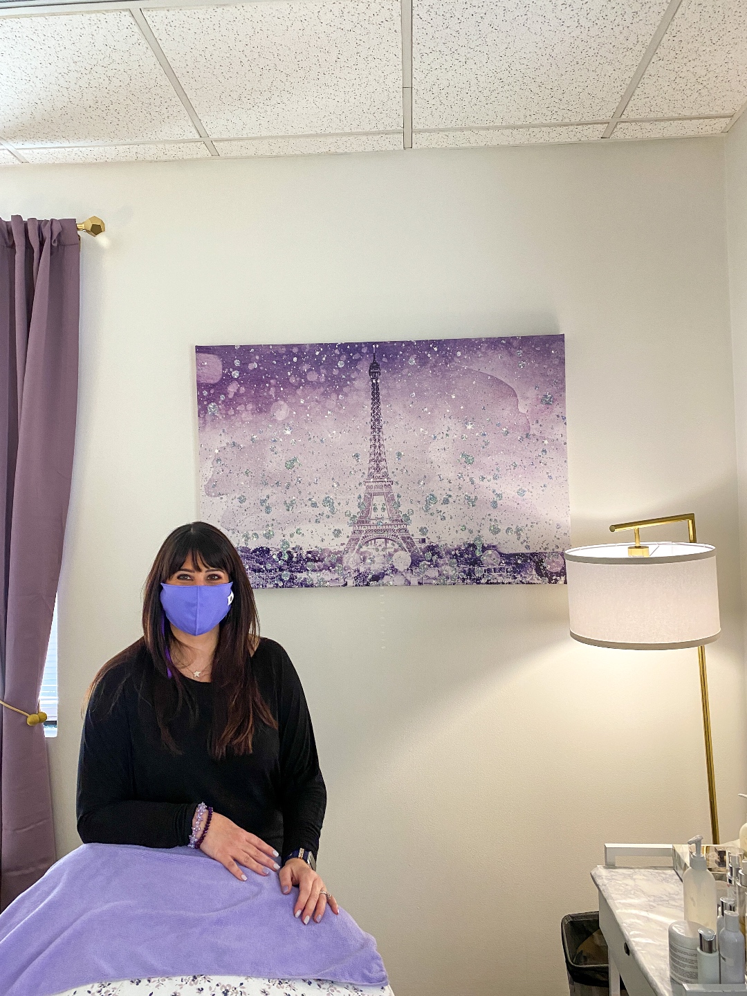 Valentine's Day Gift Guide by popular NC lifestyle blog, I'm Fixin' To: image of a woman wearing a all black outfit and purple face mask and standing in a room decorated with purple drapes, and a purple art print of the Eiffel Tower. 