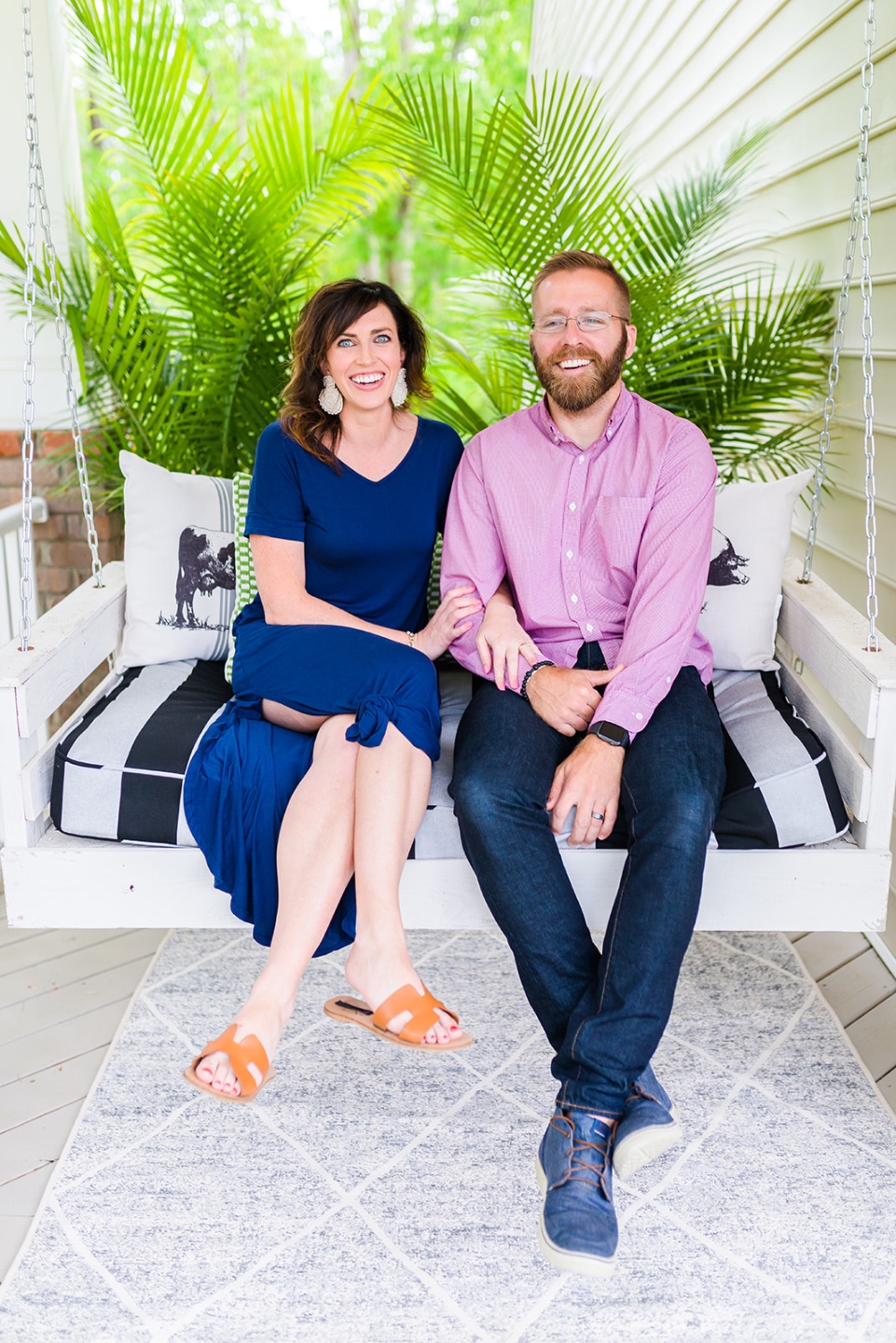 How to Make Your Home Cozy by popular NC life and style blog, I'm Fixin' To: image of a man and woman sitting together on a porch swing with a black and white stripe cushion and black and white throw pillows. 