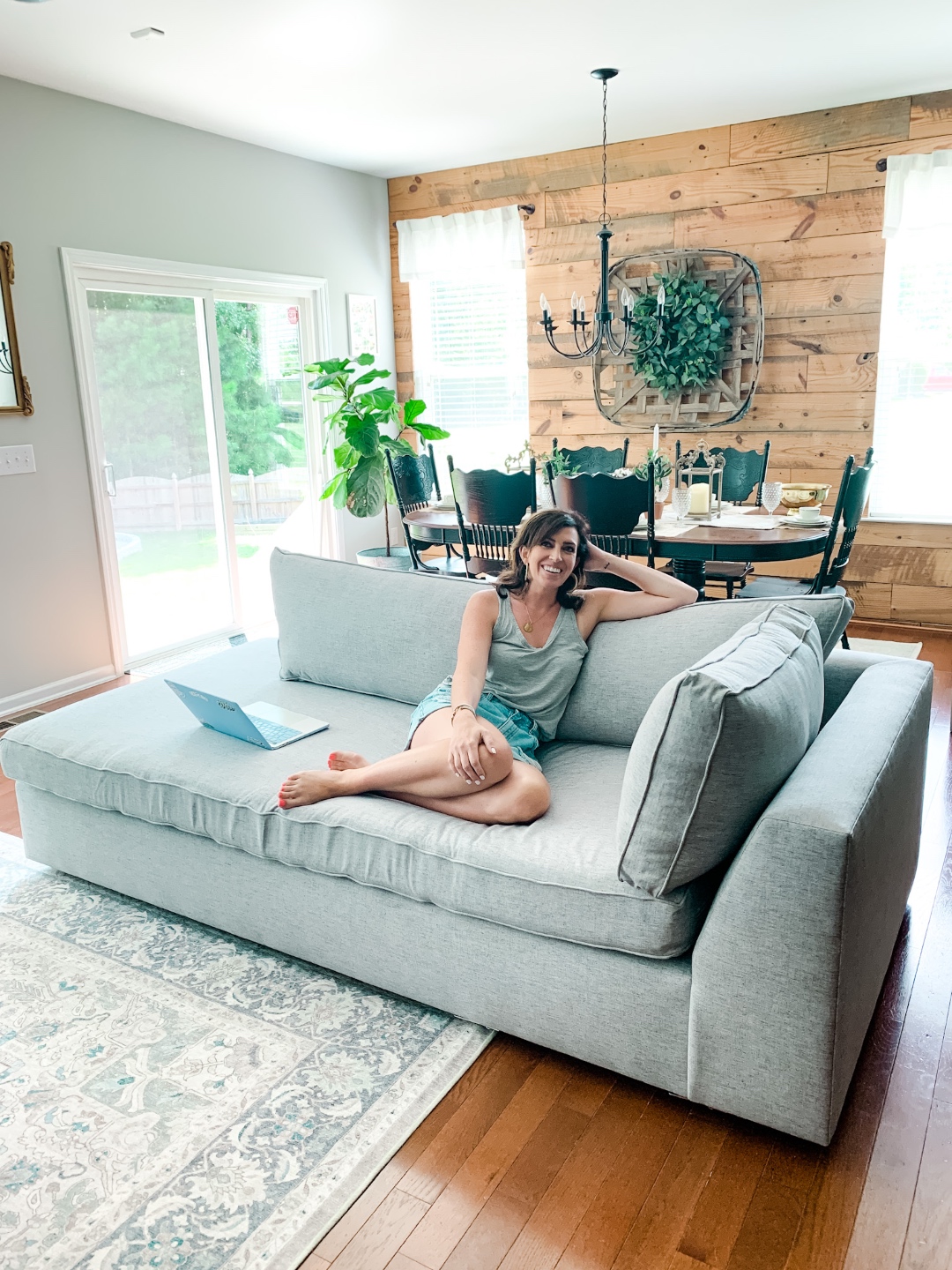 How to Make your Home Cozy: 10 Easy Ways - I'm Fixin' To - @imfixintoblog |How to Make Your Home Cozy by popular NC life and style blog, I'm Fixin' To: image of a woman sitting on a grey sectional couch in front of a black dining table with black chairs and a wood shiplap accent wall. 