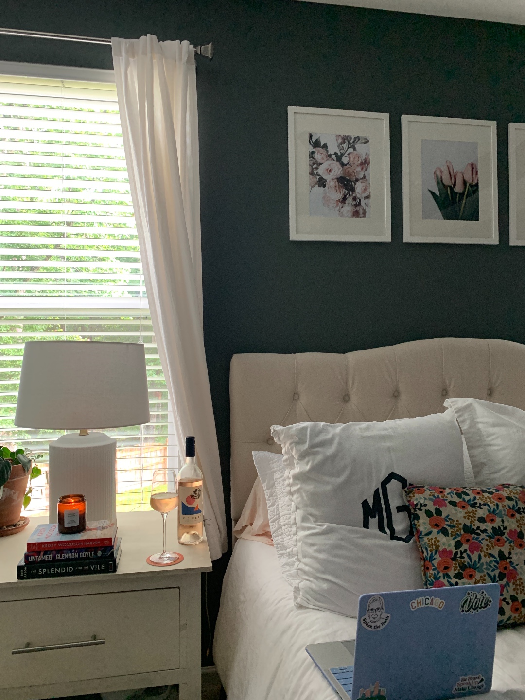 How to Make your Home Cozy: 10 Easy Ways - I'm Fixin' To - @imfixintoblog |How to Make Your Home Cozy by popular NC life and style blog, I'm Fixin' To: image of a bedroom with a bed with a white tuft headboard ad white bedding, floral print artwork, white night stands, white curtains, grey walls, and a serving tray set with a vase of flowers and a candle. 