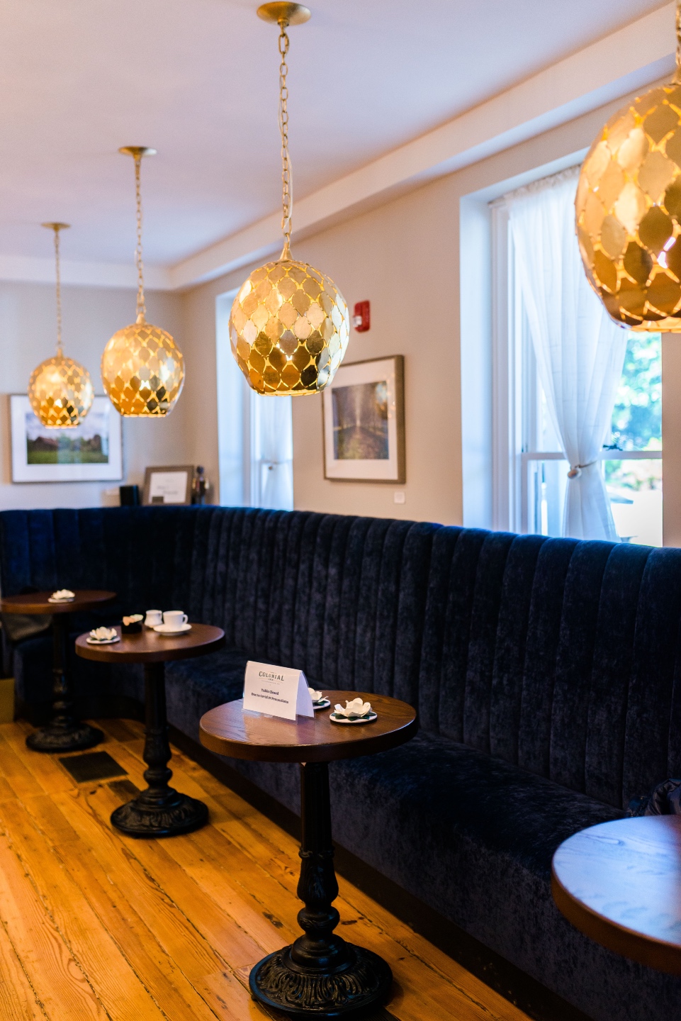 Places to Stay: The Colonial Inn in Hillsborough NC - I'm Fixin' To - @imfixintoblog |The Colonial Inn Hillsborough NC by popular NC travel blog, I'm Fixin' To: image of a black velvet bench, gold pendant lights, and round tables set with espresso cups.
