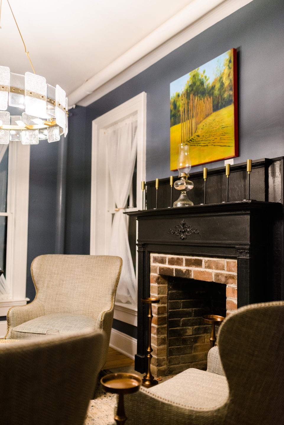 Places to Stay: The Colonial Inn in Hillsborough NC - I'm Fixin' To - @imfixintoblog |The Colonial Inn Hillsborough NC by popular NC travel blog, I'm Fixin' To: image of a sitting area with a blue wall, brick fireplace, round gold coffee table, and grey fabric wingback chairs.