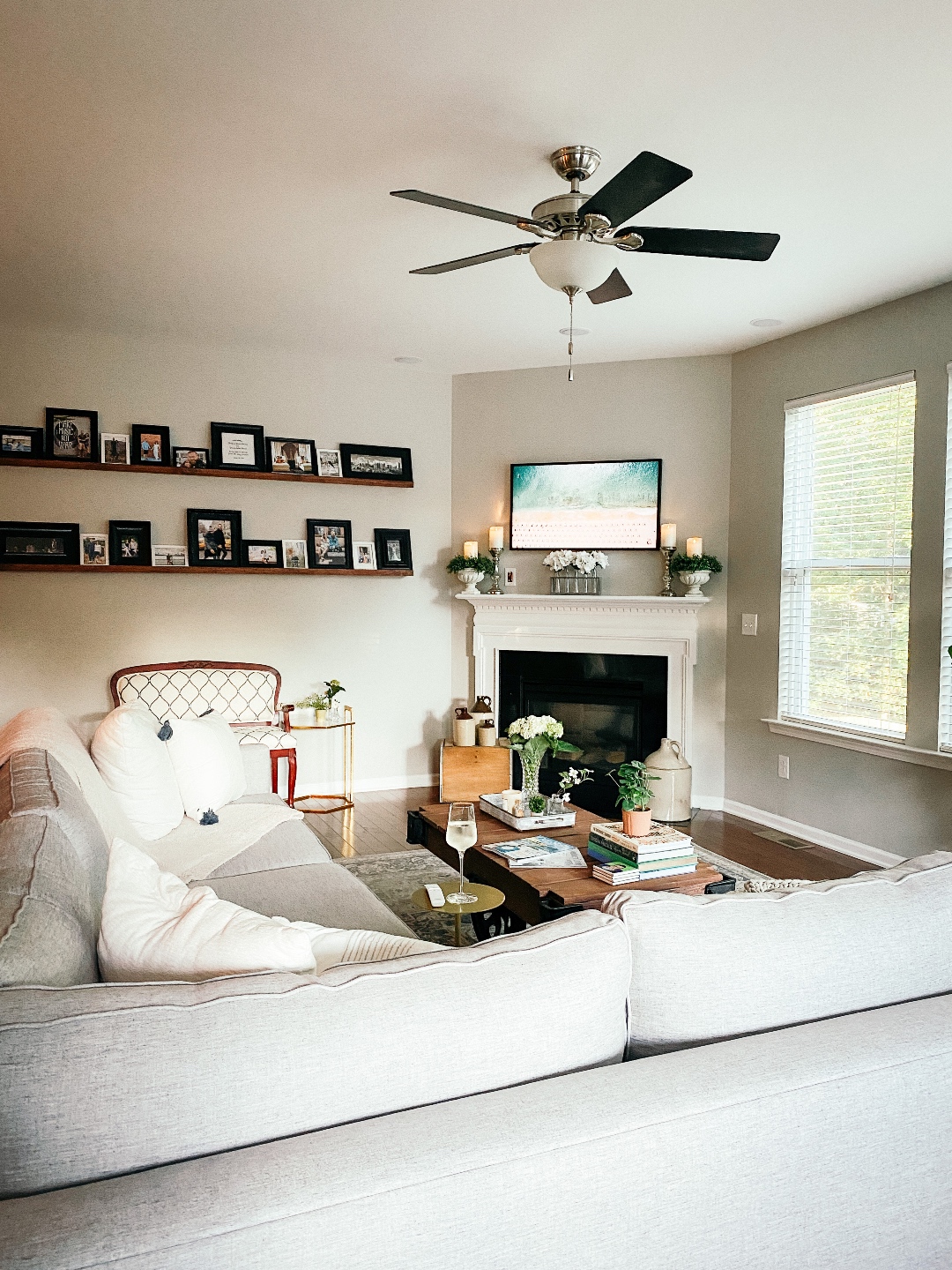 Room Reveal: Blue and Gray Living Room Ideas - I'm Fixin' To - @imfixintoblog | Blue and Grey Living Room Ideas by popular NC life and style blog, I'm Fixin' To: image of a living room decorated with a blue and white rug runner, light wood sofa table, house plants, floating wood shelves with black picture frames, white pillar candles, wooden picnic basket, blue and white floral wallpaper, and grey sectional couch. 