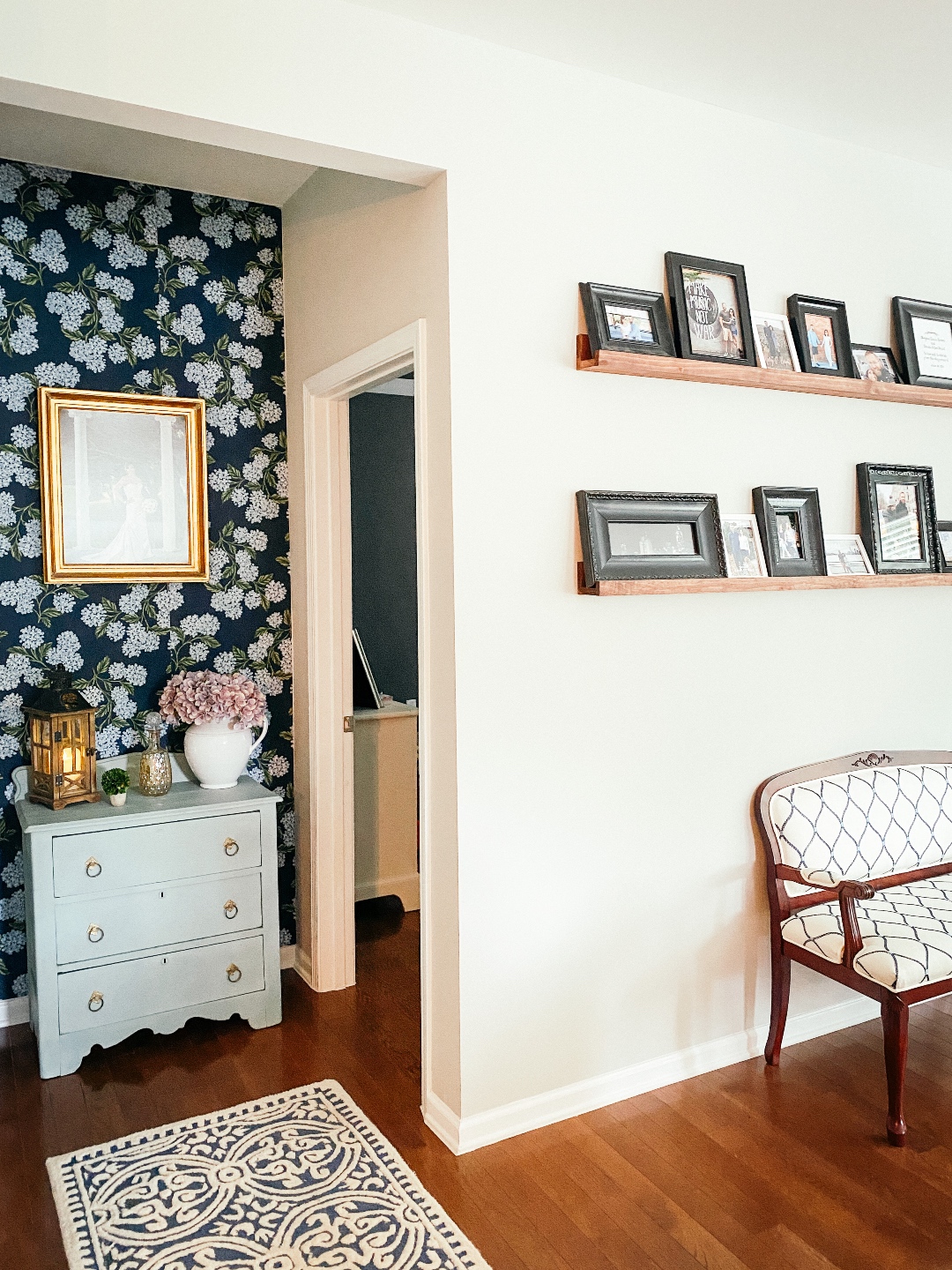 Room Reveal: Blue and Gray Living Room Ideas - I'm Fixin' To - @imfixintoblog | Blue and Grey Living Room Ideas by popular NC life and style blog, I'm Fixin' To: image of a living room decorated with a blue and white rug runner, floating wood shelves with black picture frames, white pillar candles, wooden picnic basket, blue and white floral wallpaper, blue and white armchair, and light blue dresser. 