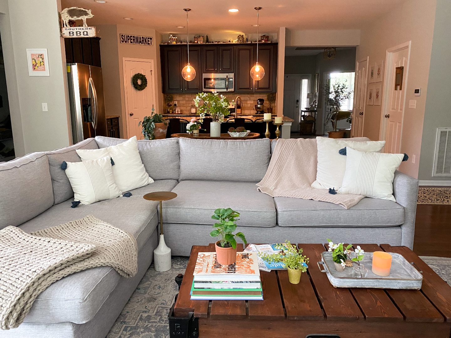 Room Reveal: Blue and Gray Living Room Ideas - I'm Fixin' To - @imfixintoblog | Blue and Grey Living Room Ideas by popular NC life and style blog, I'm Fixin' To: image of a living room decorated with a blue and white rug runner, light wood sofa table, house plants, floating wood shelves with black picture frames, white pillar candles, wooden picnic basket, blue and white floral wallpaper, and cream cable knit throw blanket. 