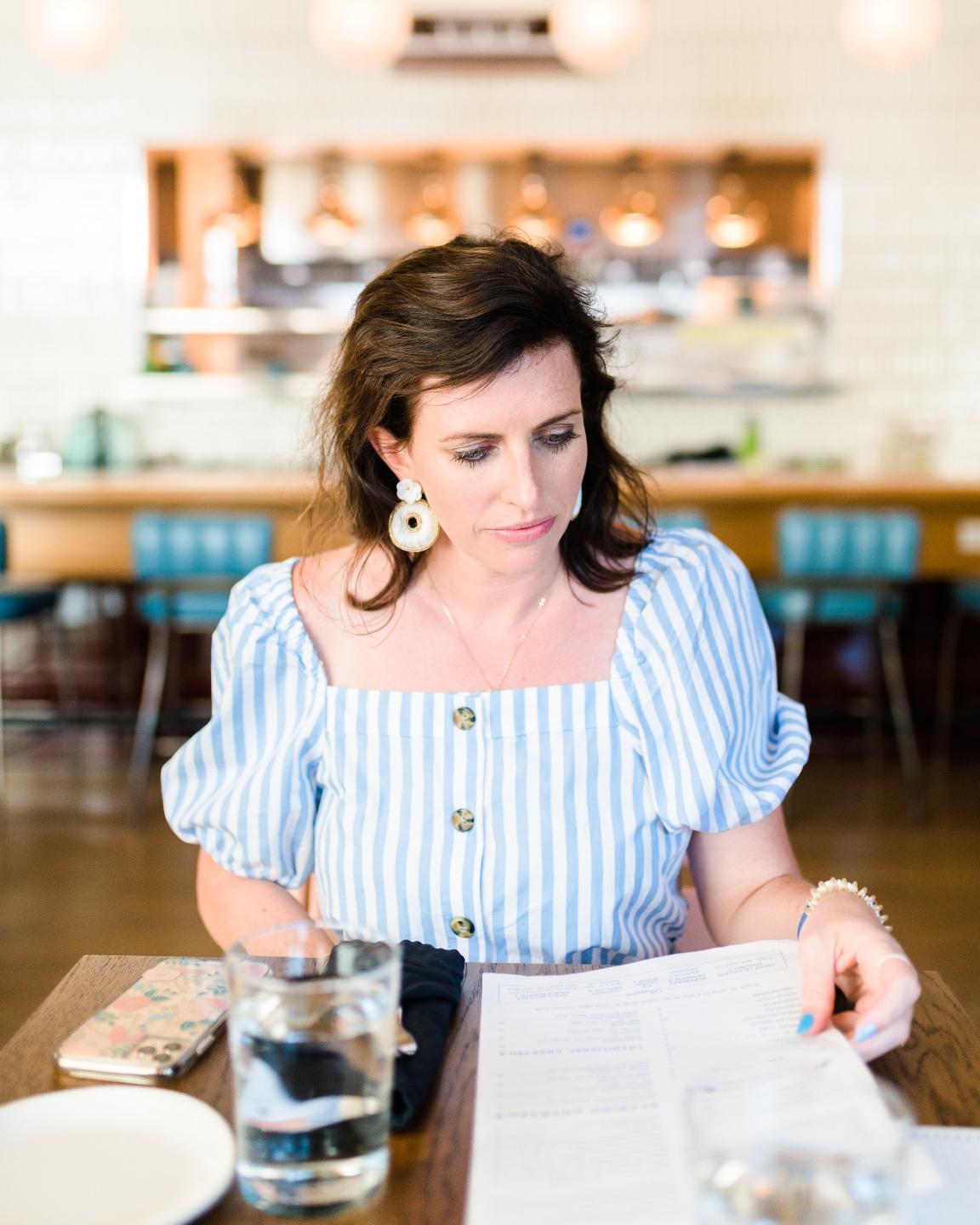 A Review of Seabird in Wilmington NC - I'm Fixin' To - @imfixintoblog | Seabird Wilmington NC by popular NC travel blog, I'm Fixin' To: image of a woman wearing a blue and white stripe dress, sitting at a table, and looking at a menu. 