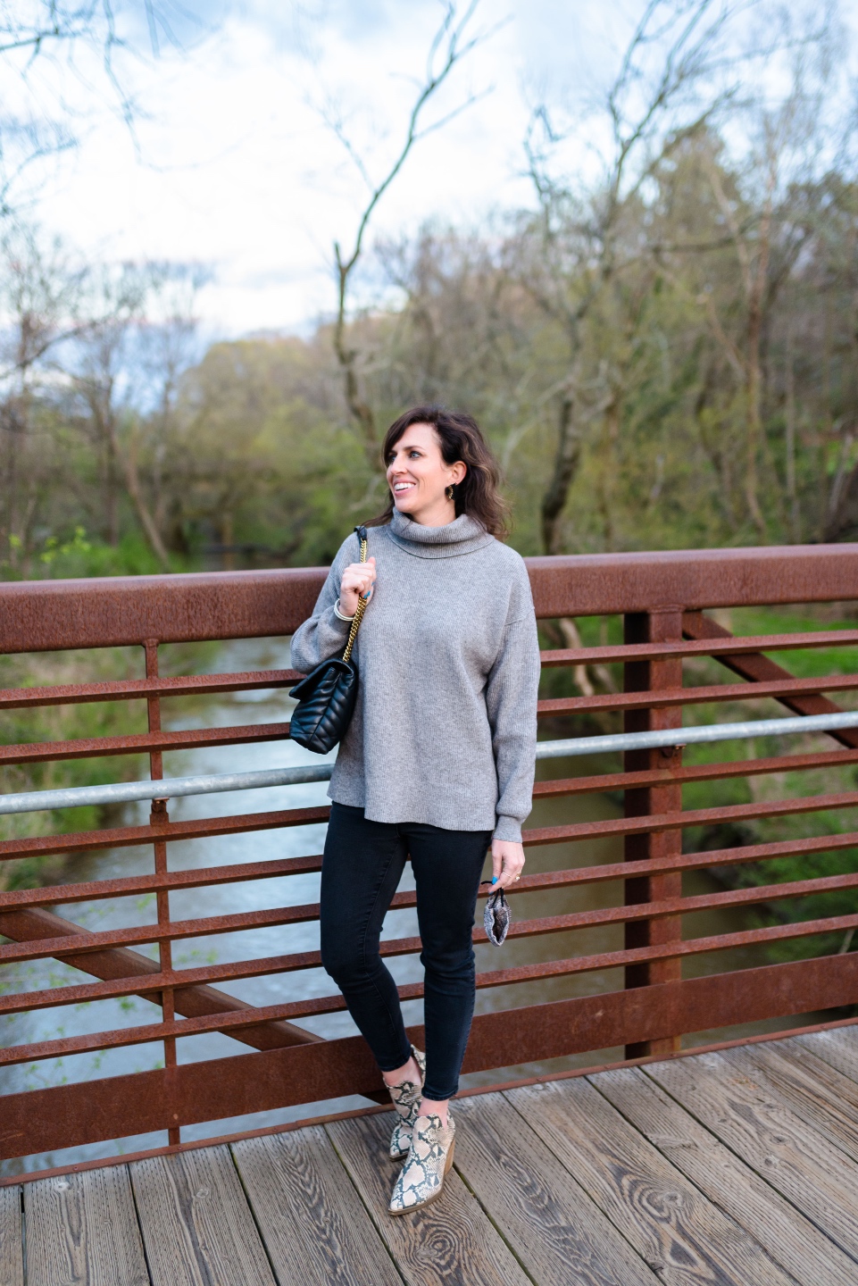 An Update on My North Carolina 100 County Tour - I'm Fixin' To - @imfixintoblog | Things to do in North Carolina by popular NC travel blog, I'm Fixin' To: image of a woman wearing a grey turtle neck sweater, black leggings, and snake print ankle boots while standing on a bridge. 